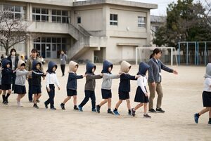 防災頭巾で列になって校庭へ避難する子どもたち