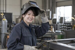 溶接面を上げて微笑む女性溶接工