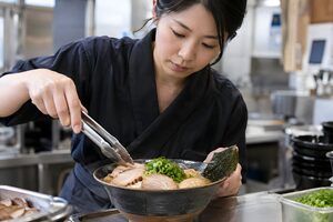 チャーシューをのせるラーメン店の店員