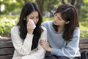 公園のベンチで友人に慰められる女性