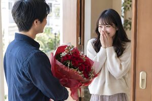 赤いバラの花束でサプライズする男性