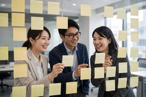 ガラス壁の付箋を囲んで笑う3人のチーム