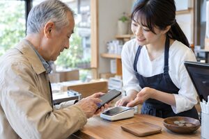 店員に教わりながらスマホで支払う高齢男性