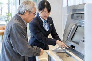 行員に手伝われてATMを使う高齢男性