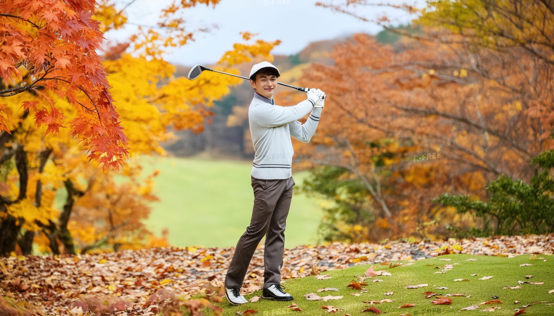 紅葉のゴルフ場でスイングをする男性