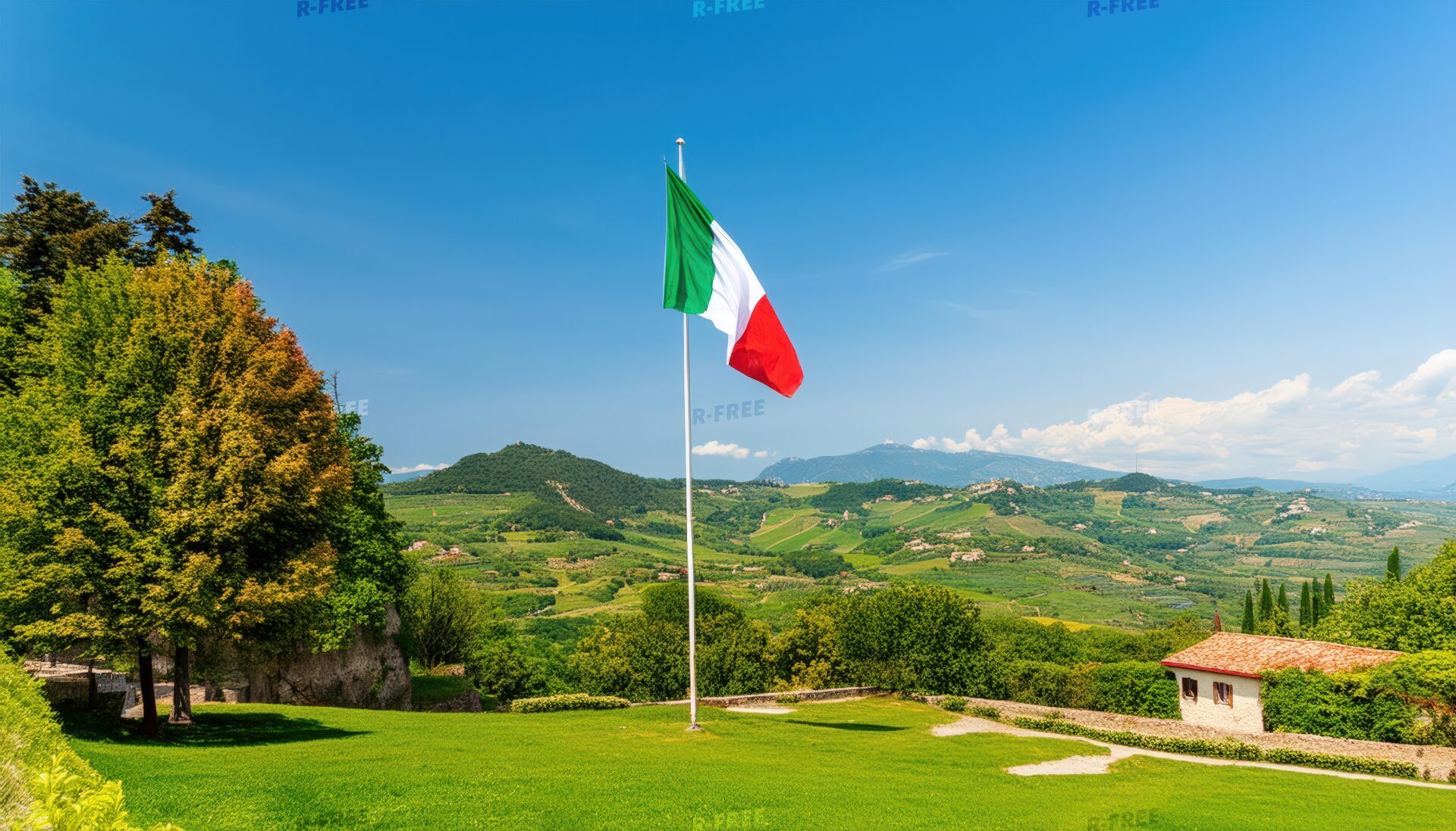 芝生と緑の丘陵を背景に風になびくイタリア国旗