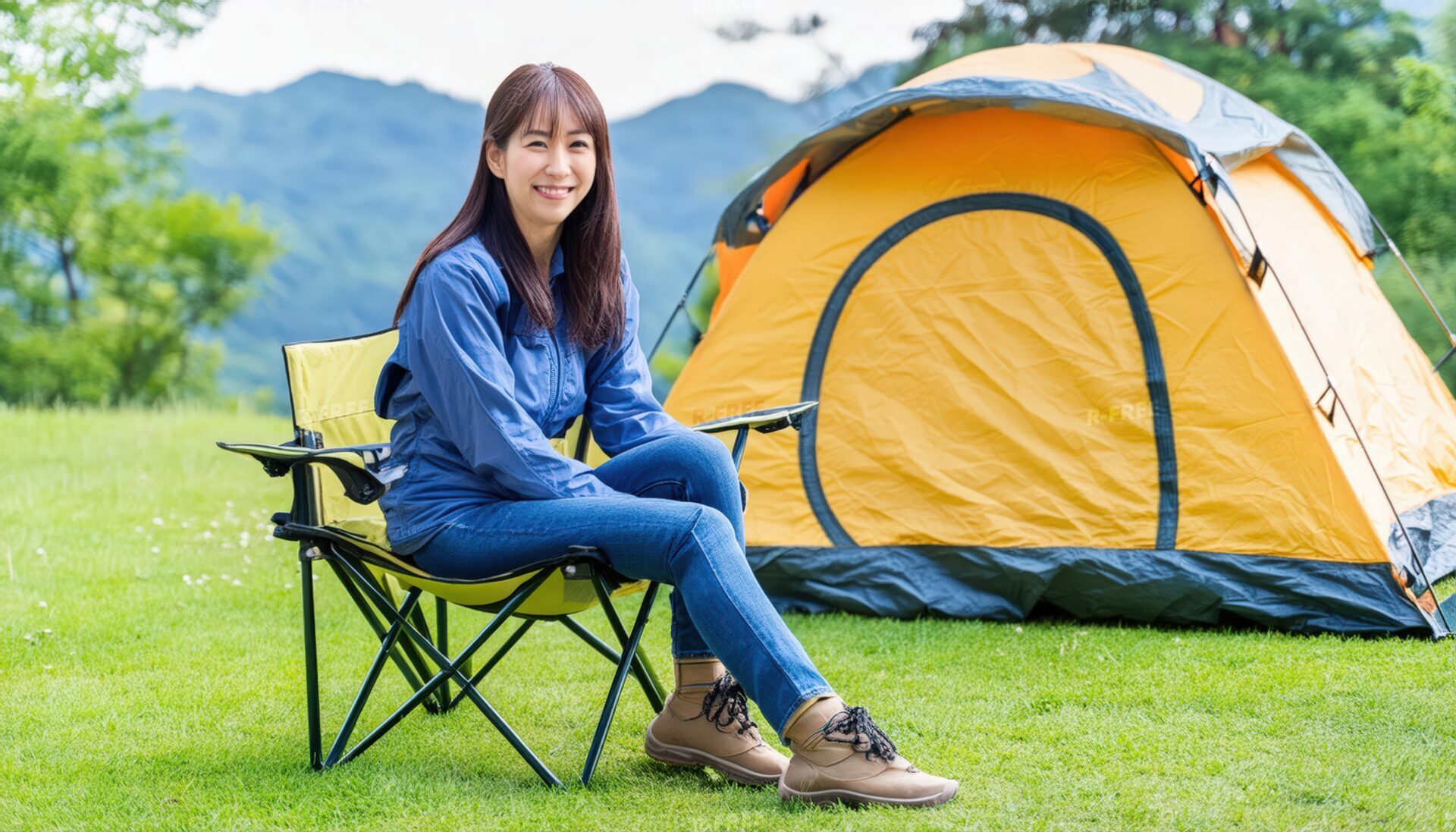 笑顔でアウトドアチェアに座る青いジャケットの女性