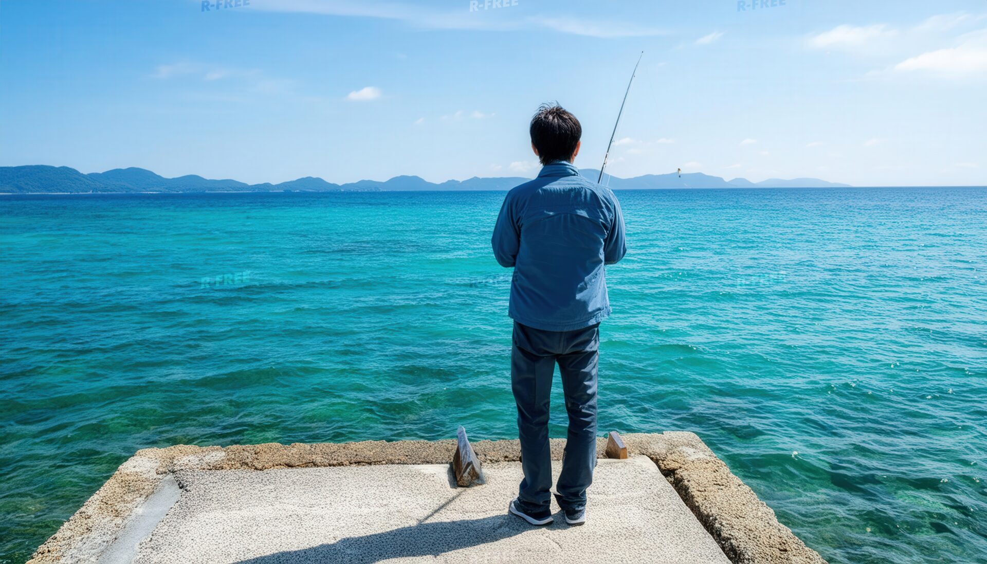 青いシャツの40代男性が海に向かい釣り竿を構える後ろ姿