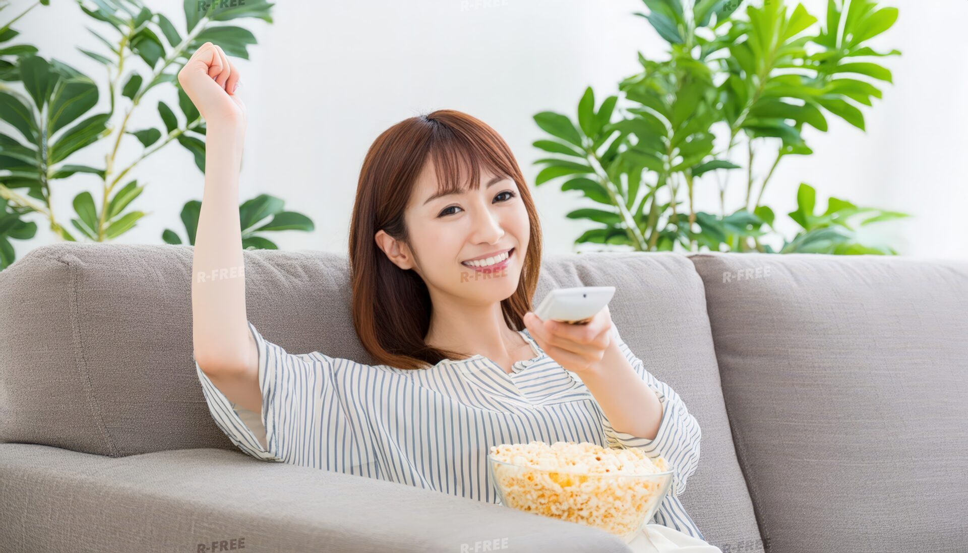 ソファでポップコーンを食べながらテレビを見る女性