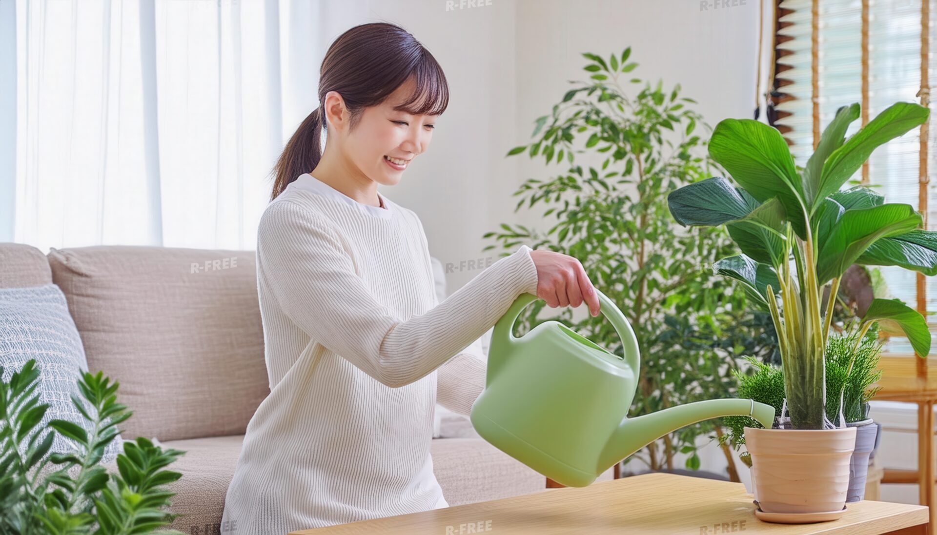 笑顔でじょうろを持ち観葉植物に水を注ぐ白いニットの女性