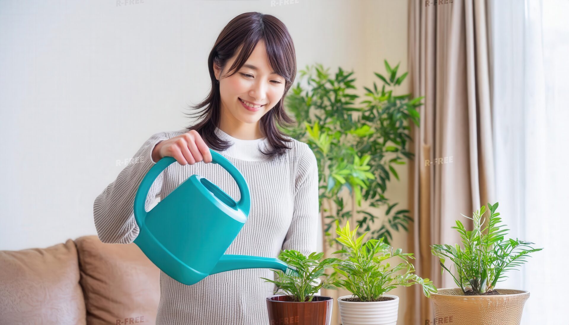 笑顔でジョウロを使い観葉植物に水をあげるベージュのニットの女性