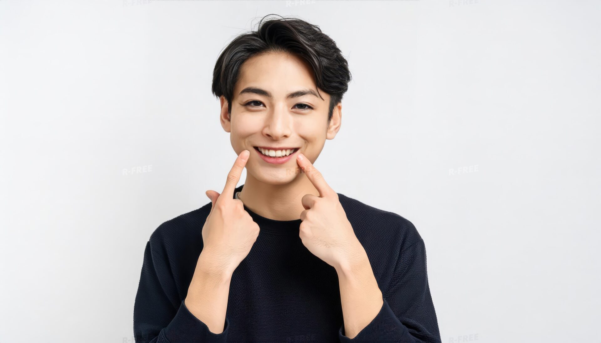 笑顔を両手で指差す黒いトップスの20代男性
