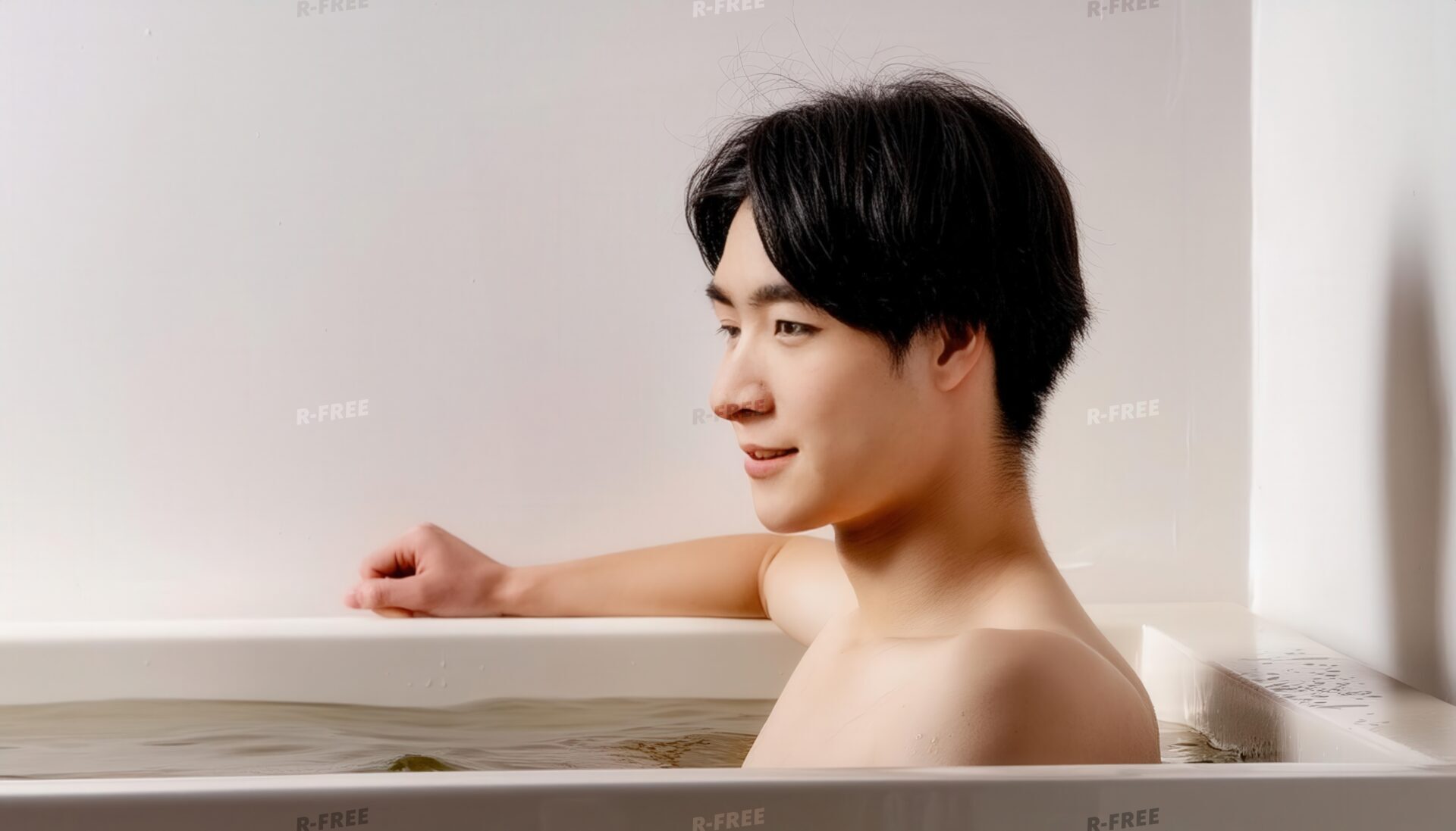 白い壁の浴室で横を向き湯船に浸かる笑顔の男性