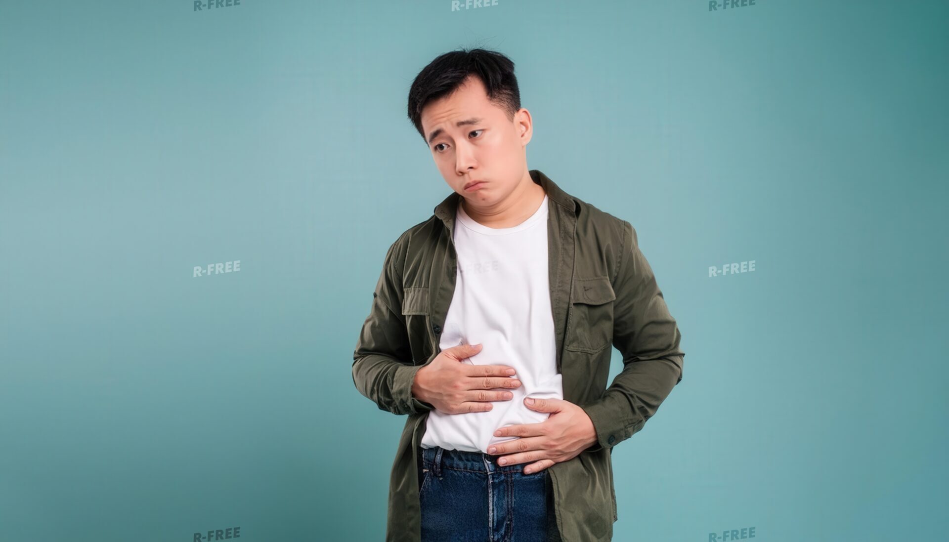 苦しそうな表情で両手でお腹を押さえるカーキシャツの男性