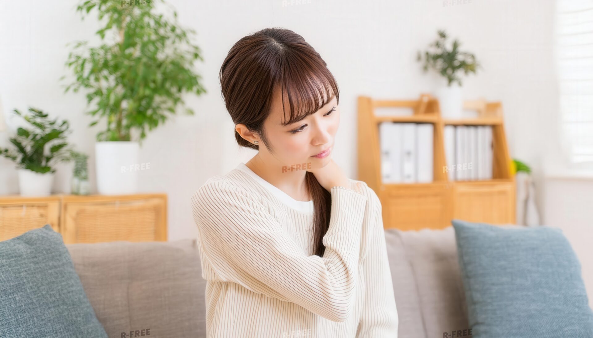肩こりで左肩を揉む白いニットの若い女性