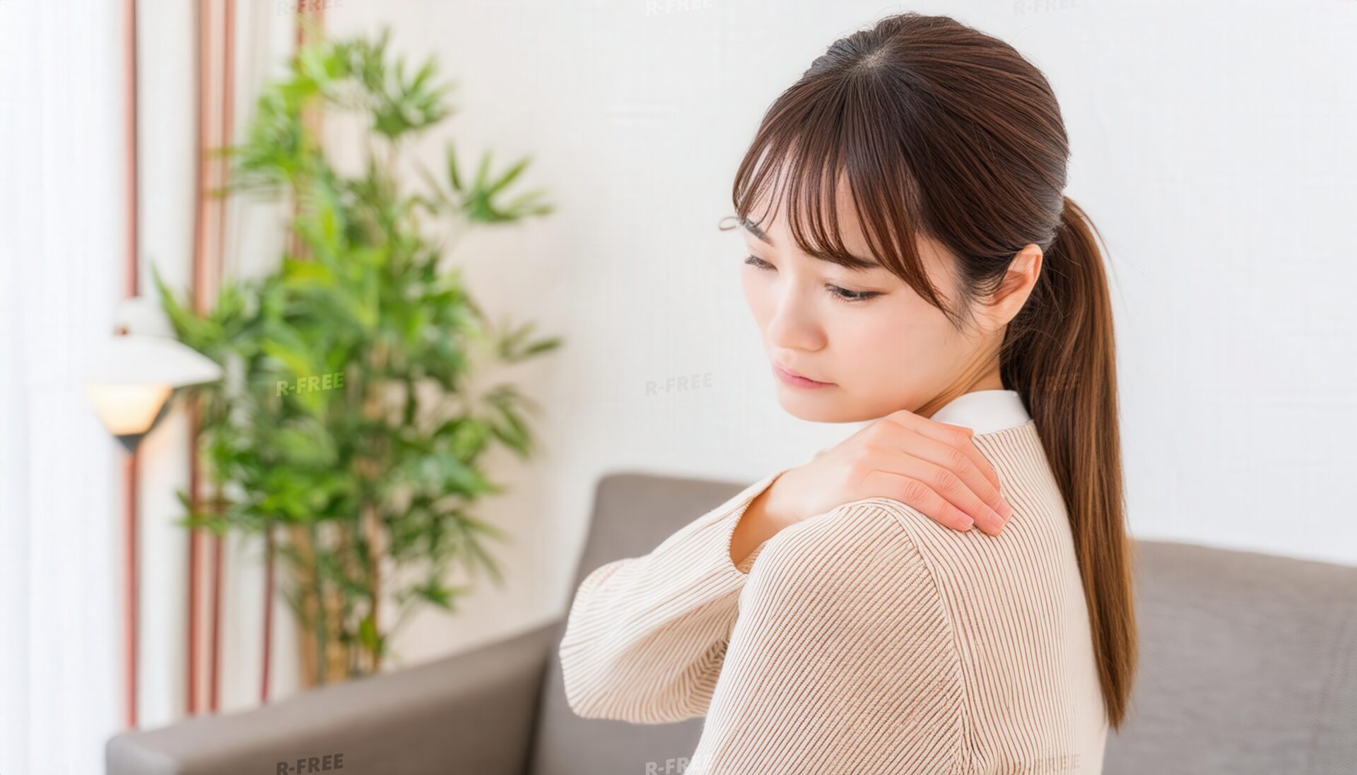 肩こりで右肩を押さえるベージュニットの女性