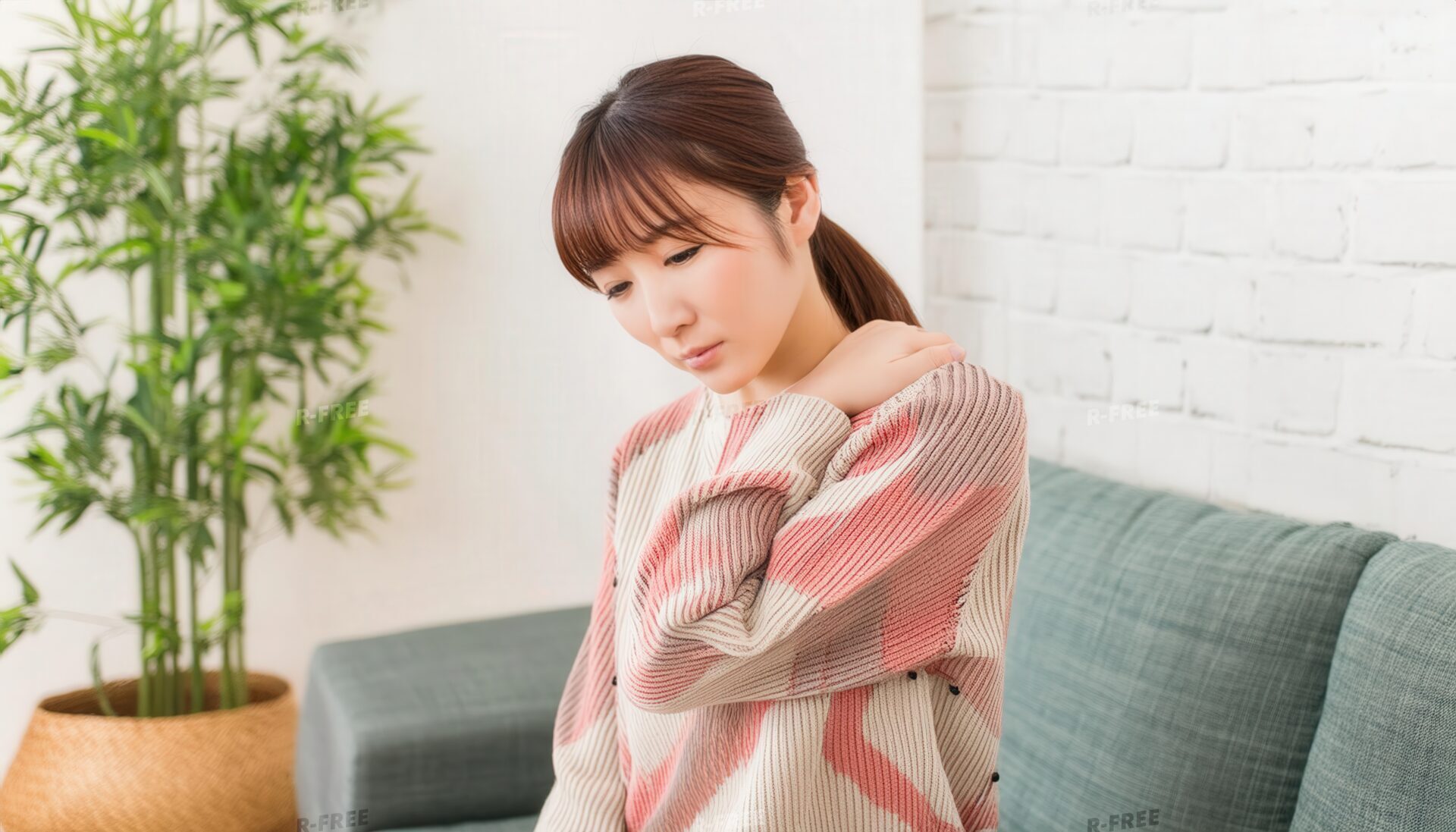 肩こりで左肩に手を添えるボーダーニットの女性