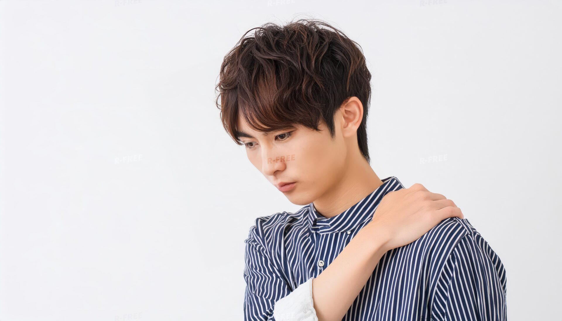 肩こりで左肩を押さえ俯くストライプシャツの20代男性