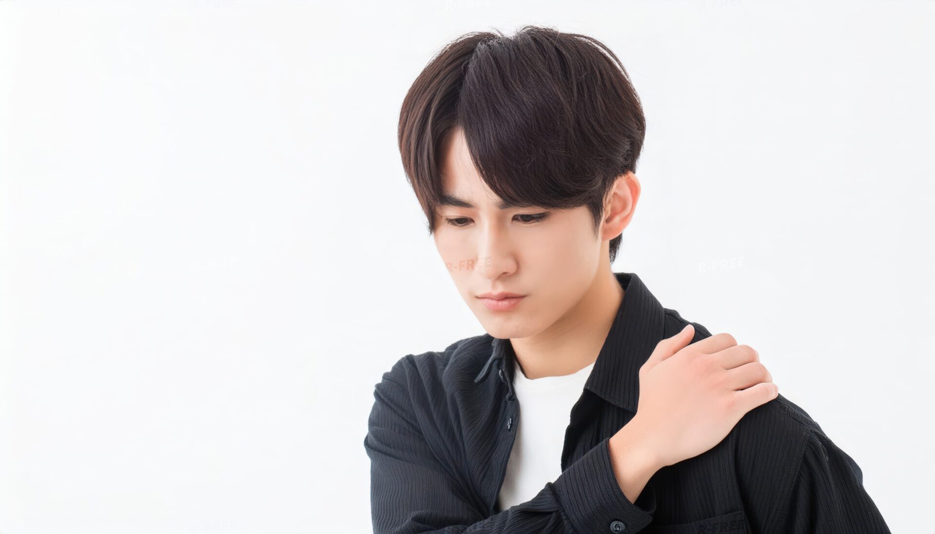 肩こりで左肩に手を置き俯く黒シャツの20代男性