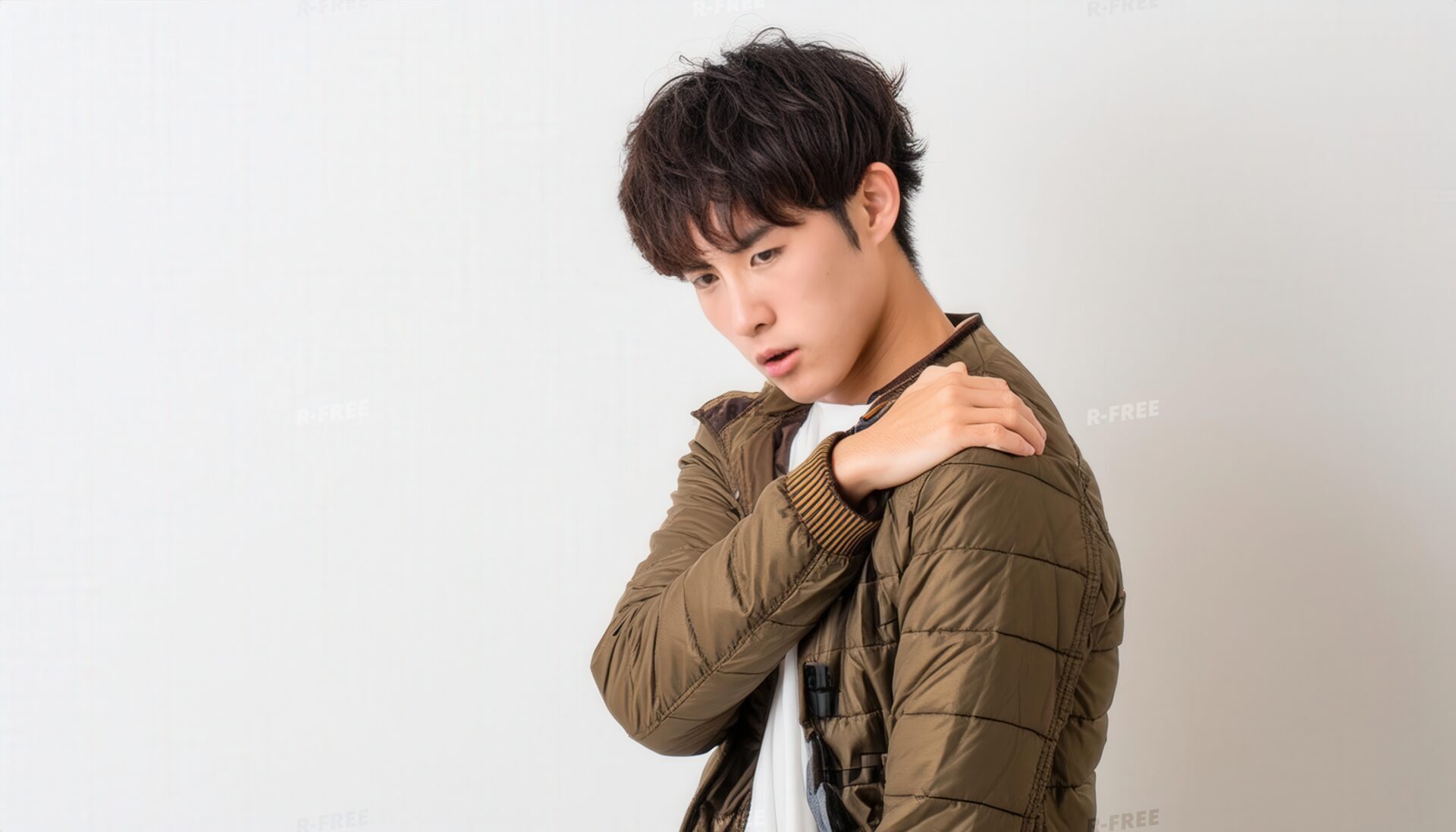 肩こりで左肩を揉む茶色ジャケットの20代男性