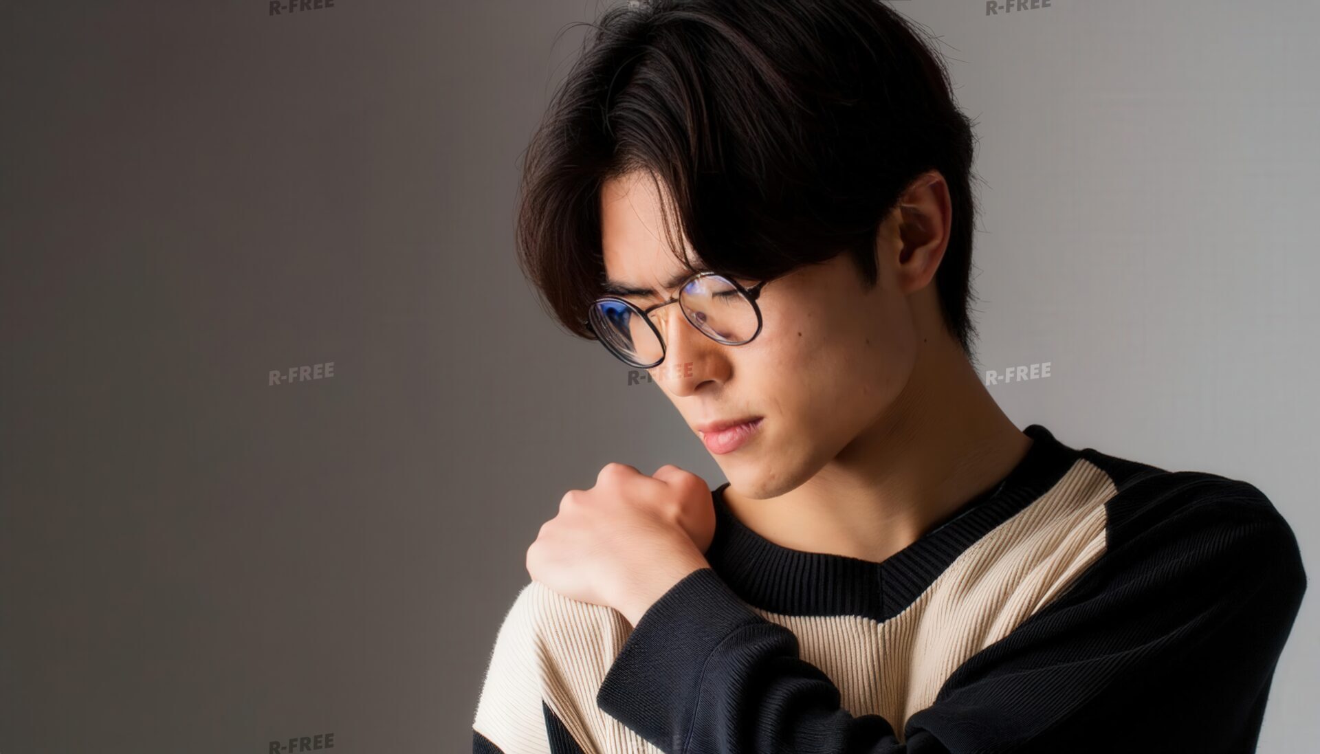 肩こりで右肩に手を当てる丸眼鏡の20代男性