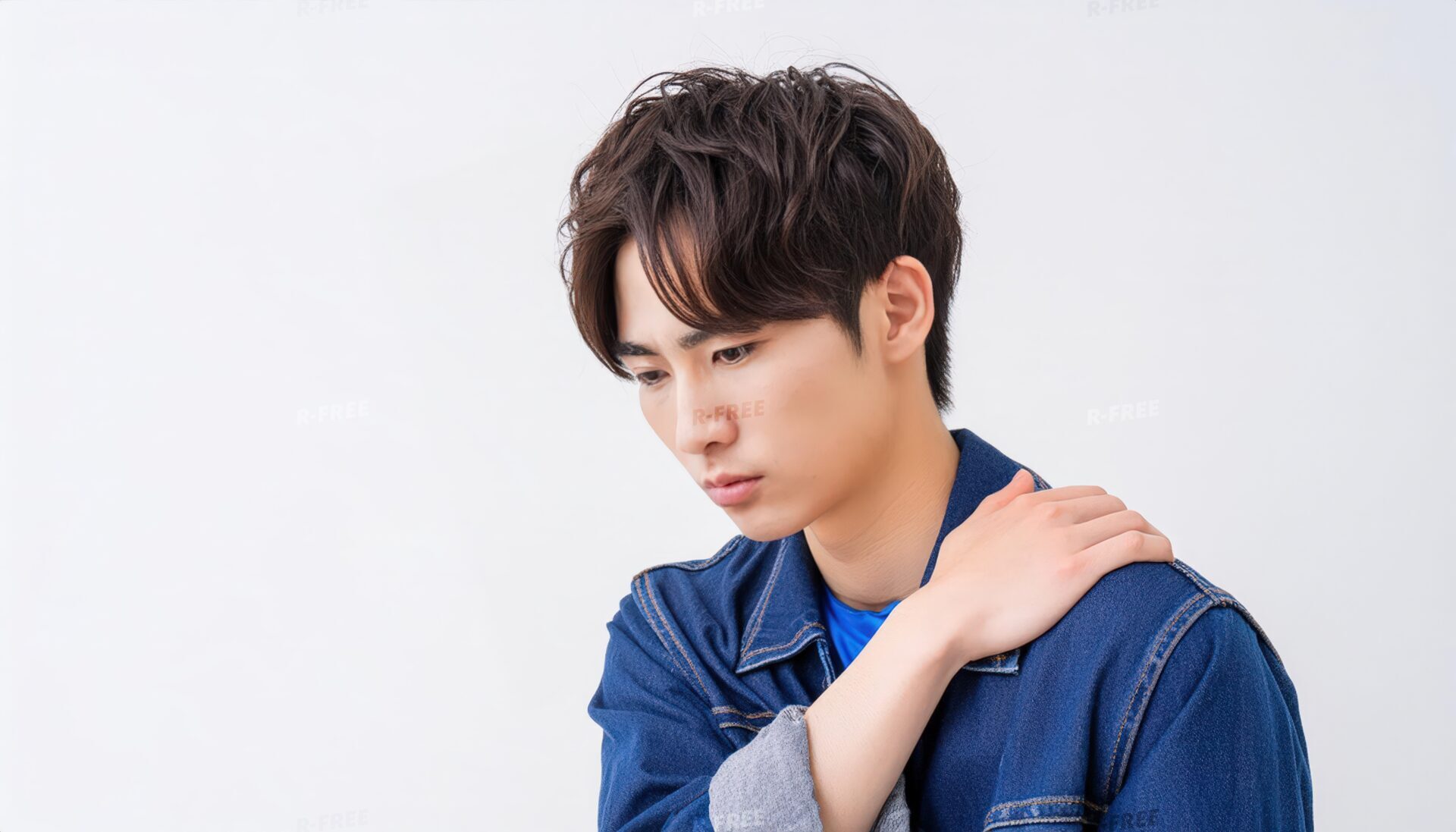 肩こりで左肩を押さえるデニムジャケットの20代男性