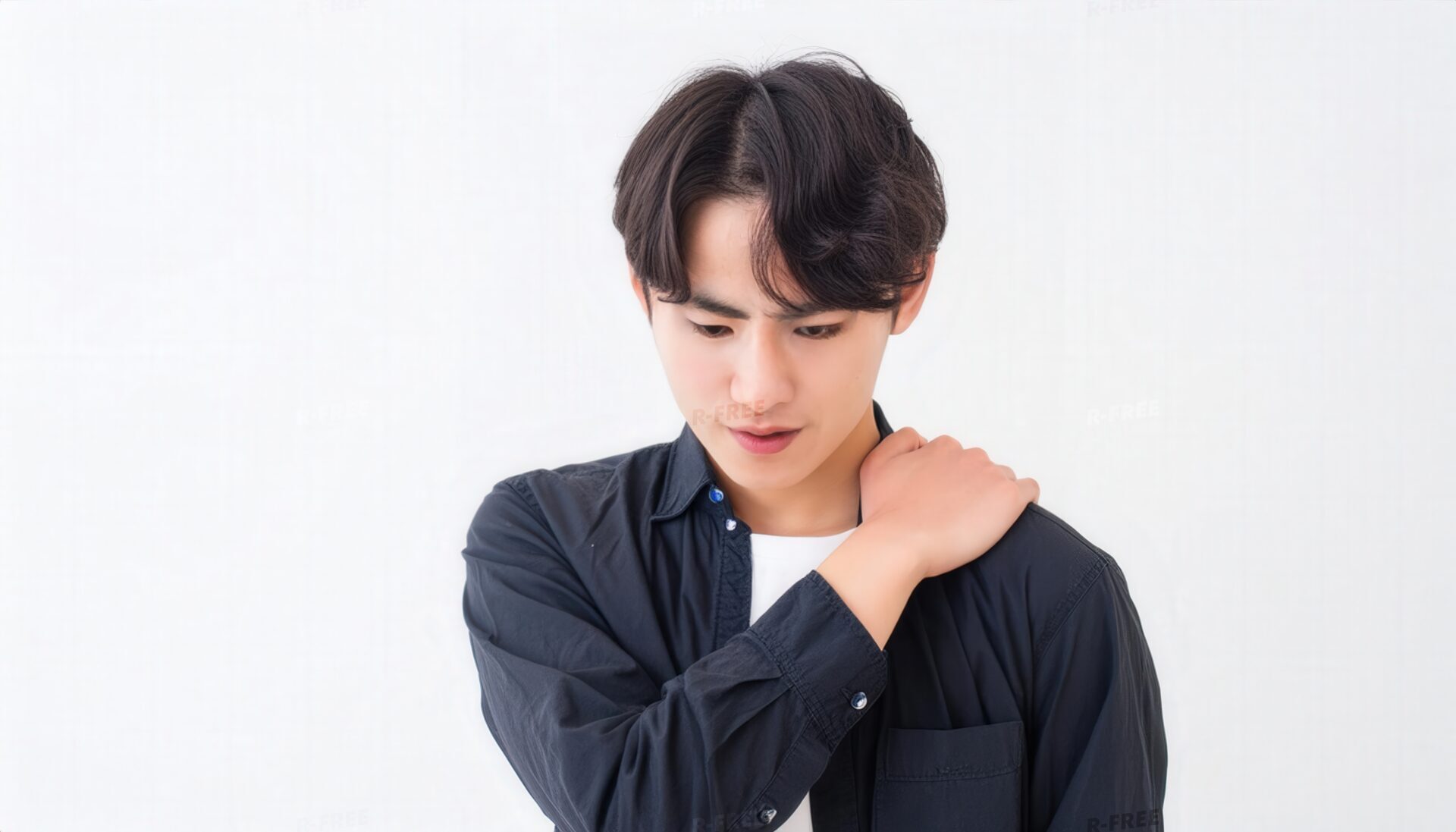 肩こりで左肩を掴み俯く紺色シャツの20代男性