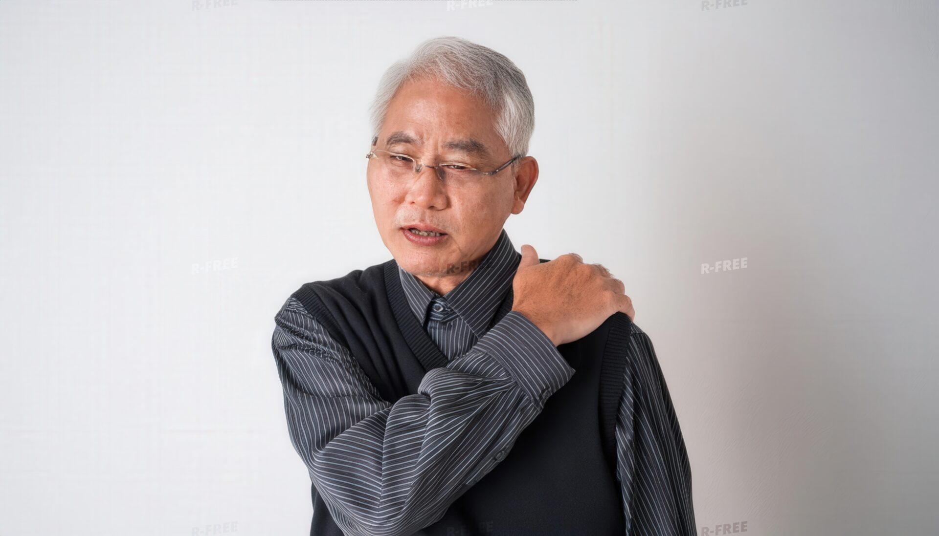 肩こりで左肩を押さえる眼鏡のシニア男性