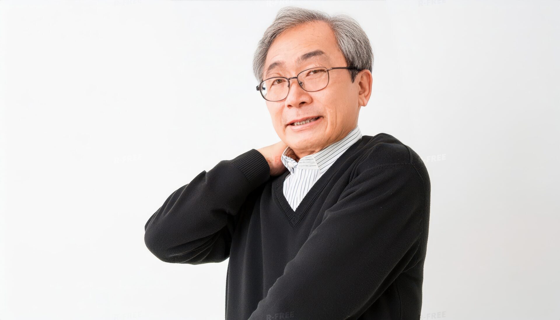 肩こりで肩に手を添え正面を見る黒セーターのシニア男性
