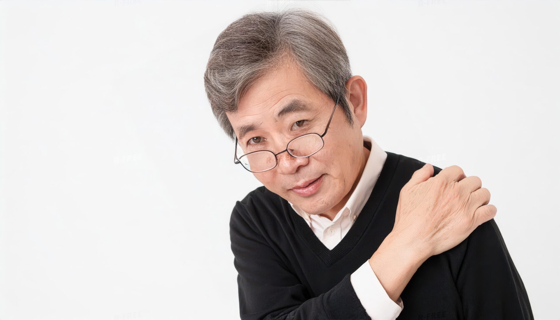 肩こりで左肩を押さえ辛そうな黒セーターのシニア男性