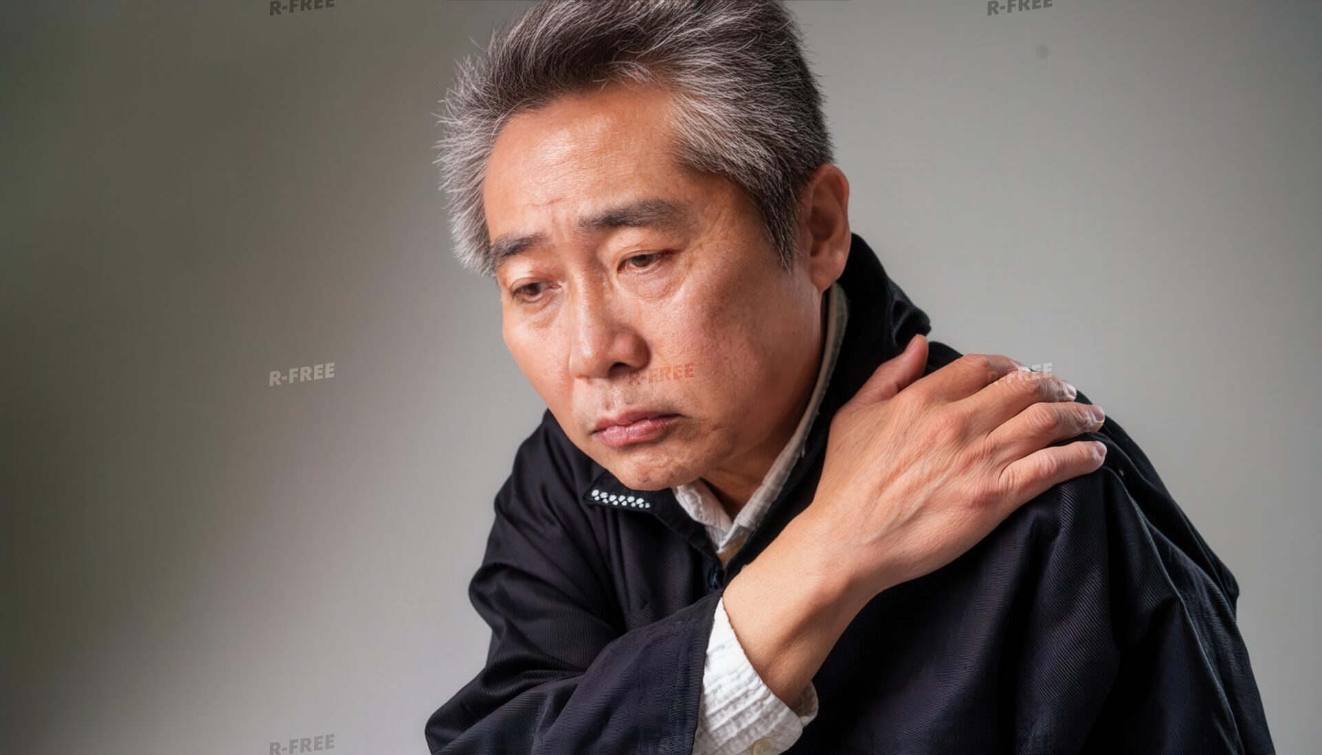 肩こりで左肩を押さえる黒い上着のシニア男性