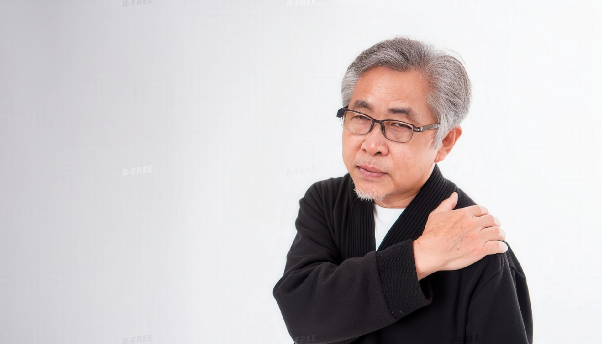 肩こりで左肩に手を置く余白構図のシニア男性