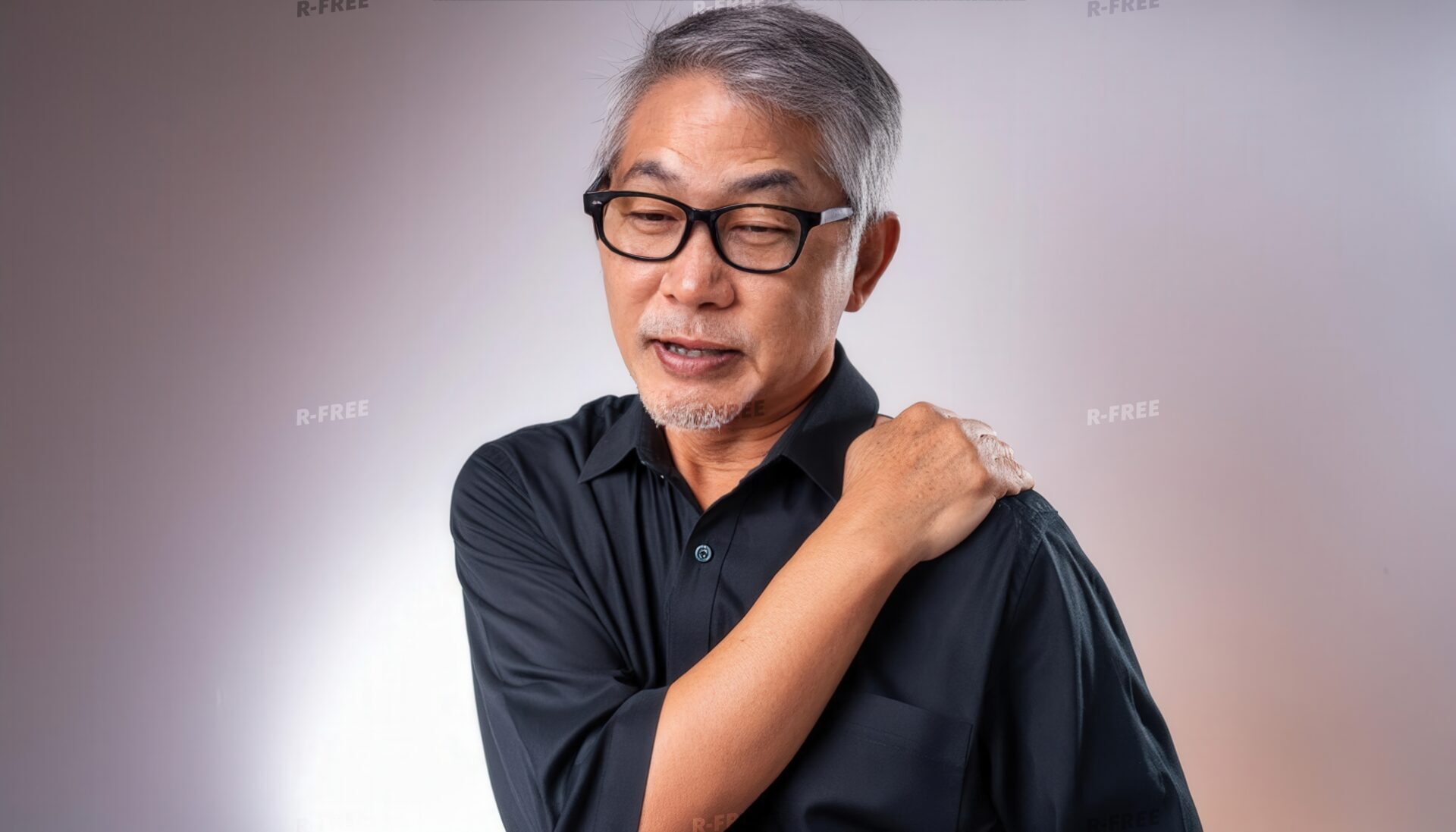 肩こりで左肩を揉む黒シャツの眼鏡シニア男性