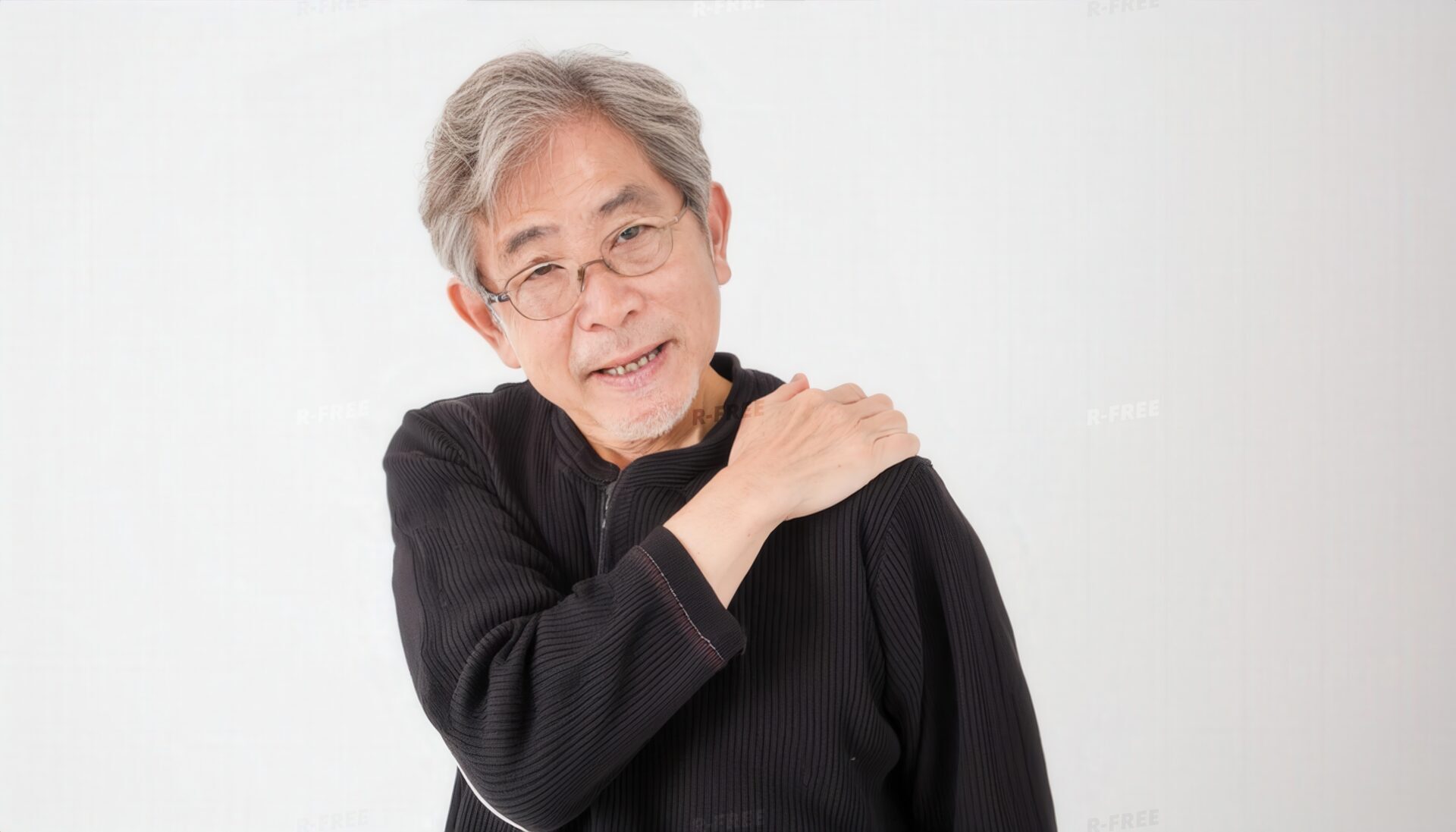 肩こりで左肩を押さえ顔をしかめる黒長袖のシニア男性
