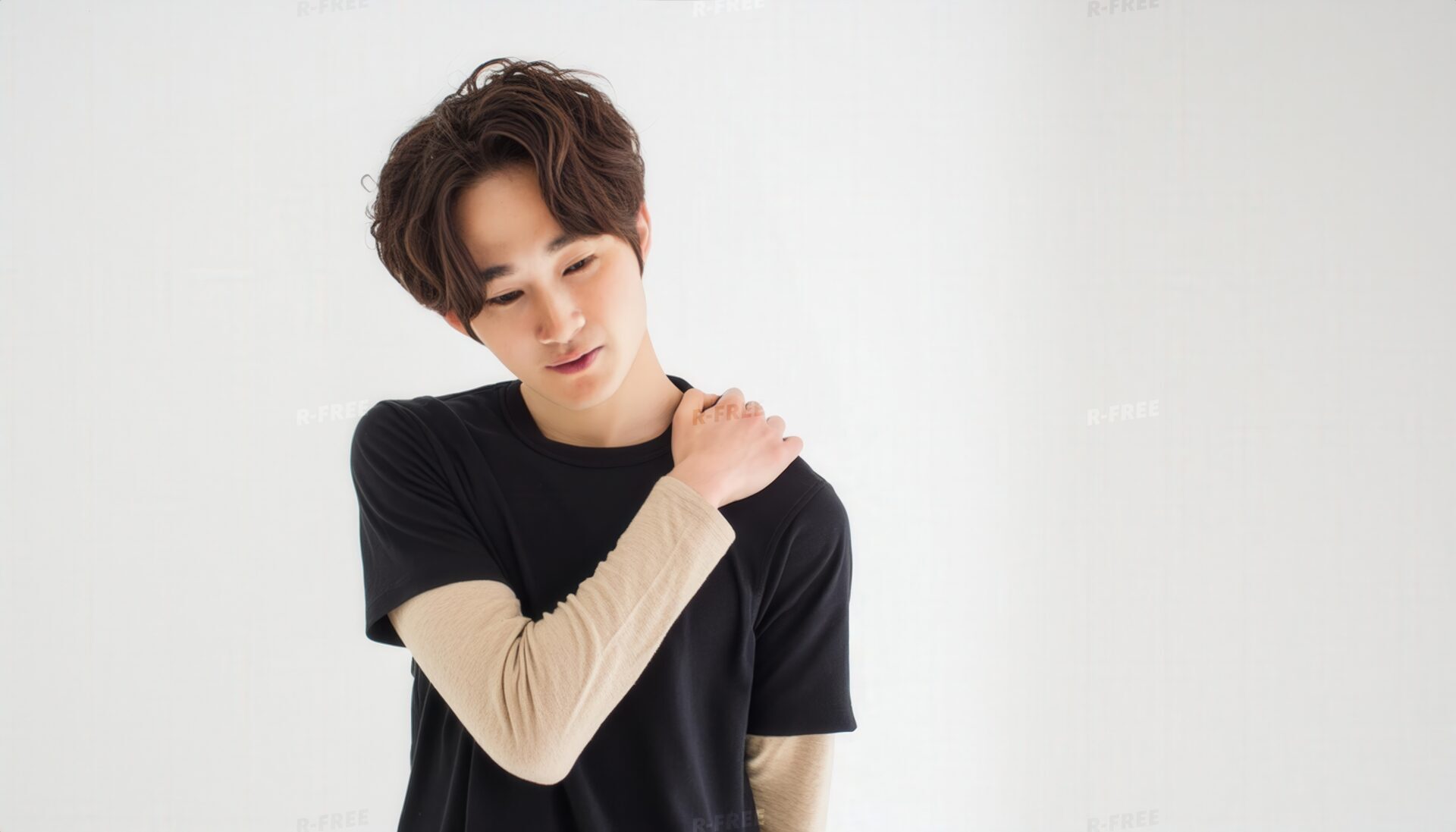 肩こりで左肩を押さえる黒Tシャツの20代男性