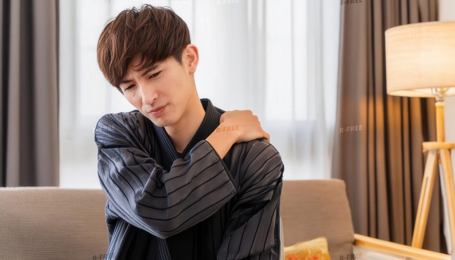 肩こりで肩を揉む部屋着姿のソファの20代男性