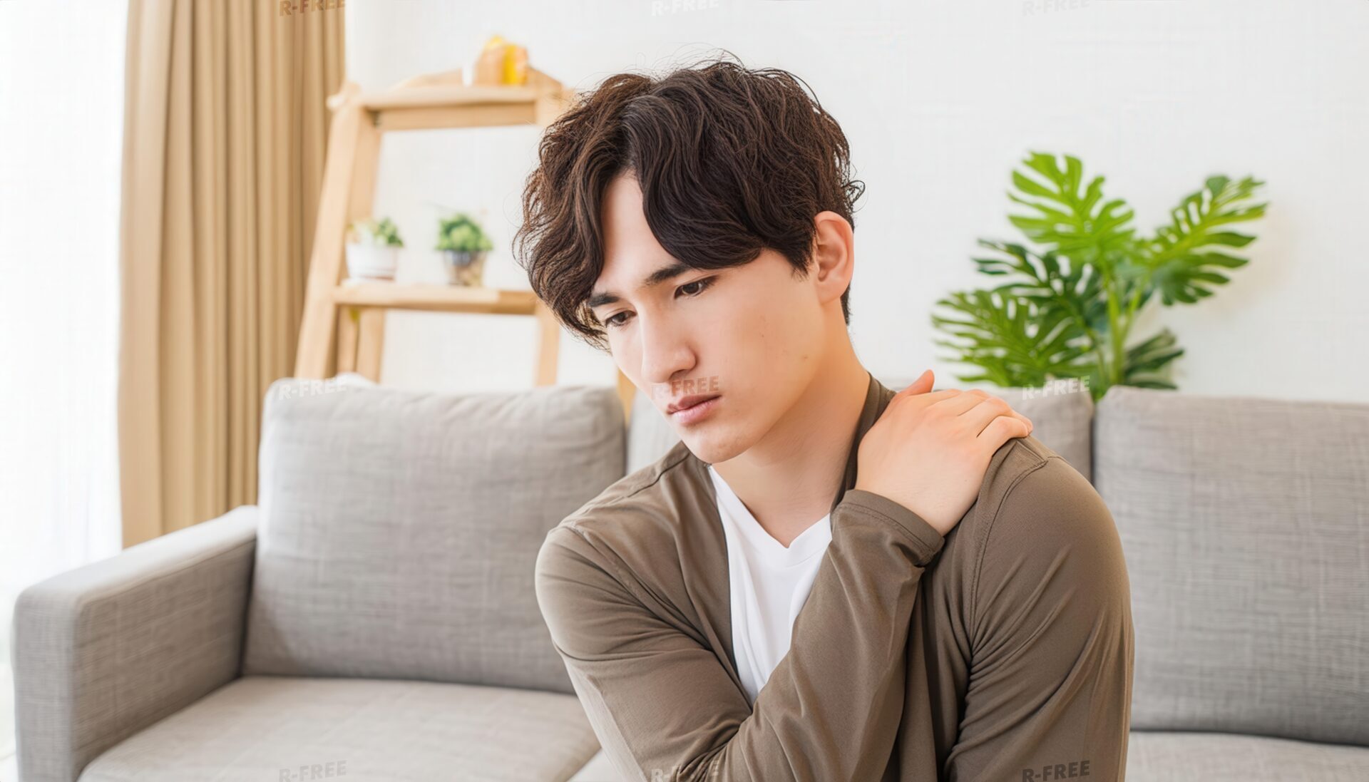 肩こりで左肩を押さえるカーディガン姿の20代男性