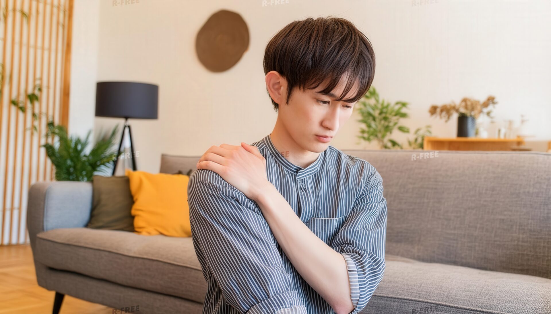 肩こりで右肩に手を置くストライプシャツの20代男性