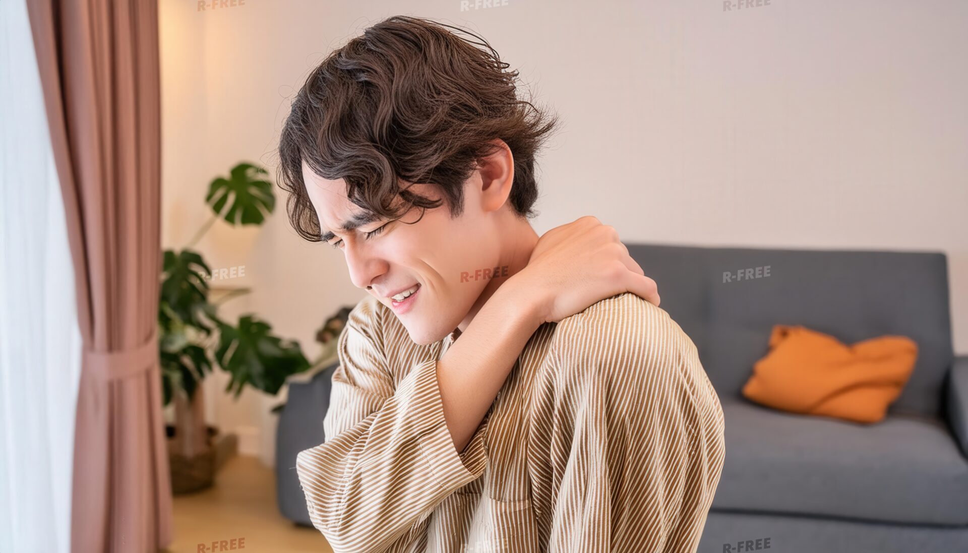 肩こりで右肩を押さえるパジャマ姿の20代男性