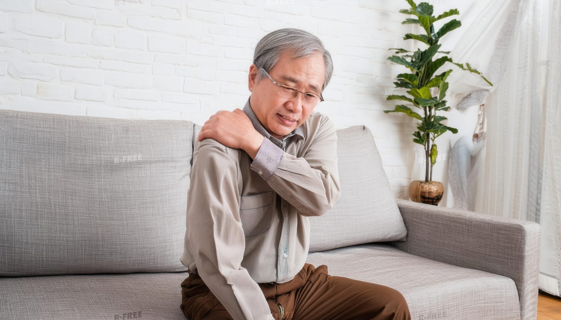 肩こりで肩を揉むグレーシャツの眼鏡シニア男性