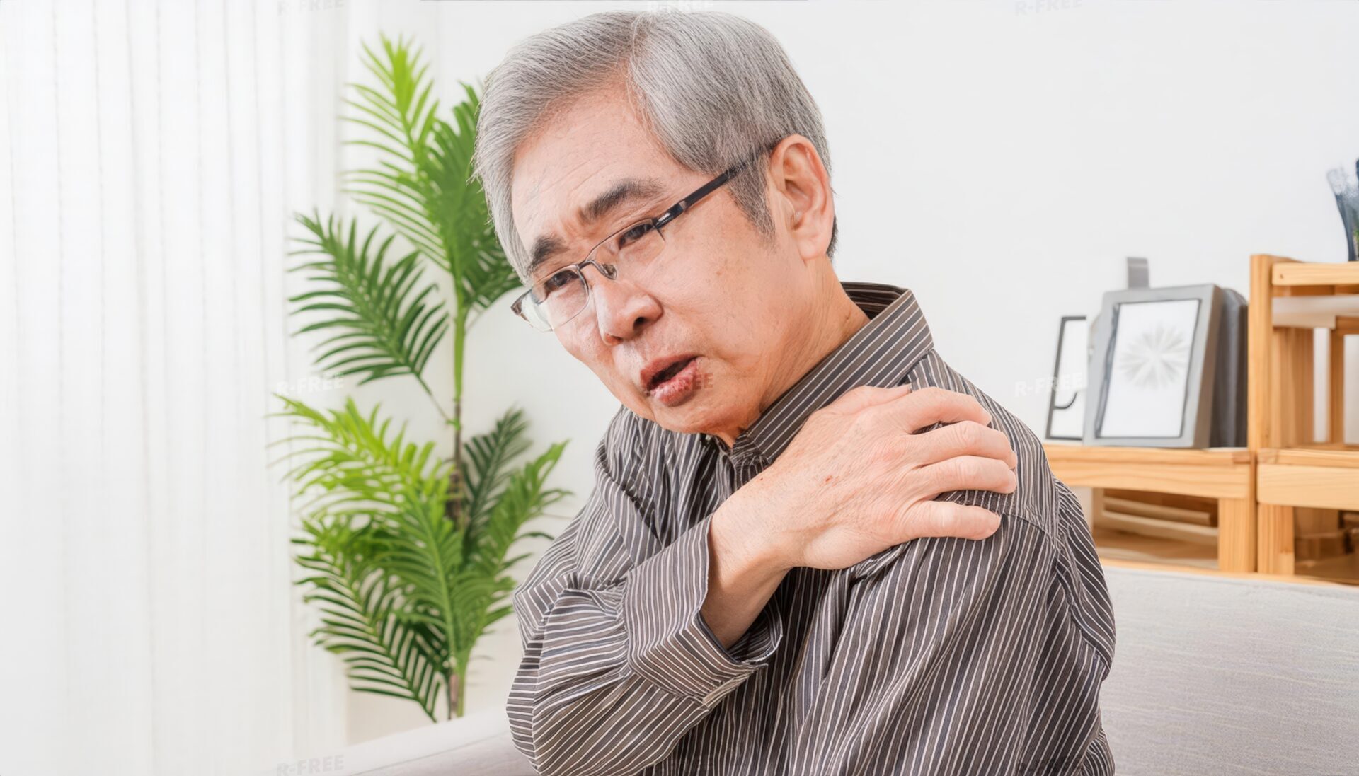肩こりで左肩を揉むストライプシャツのシニア男性