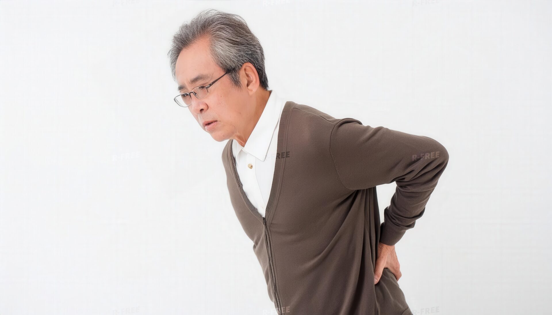 腰痛に苦しむ眼鏡の高齢男性の白壁での姿