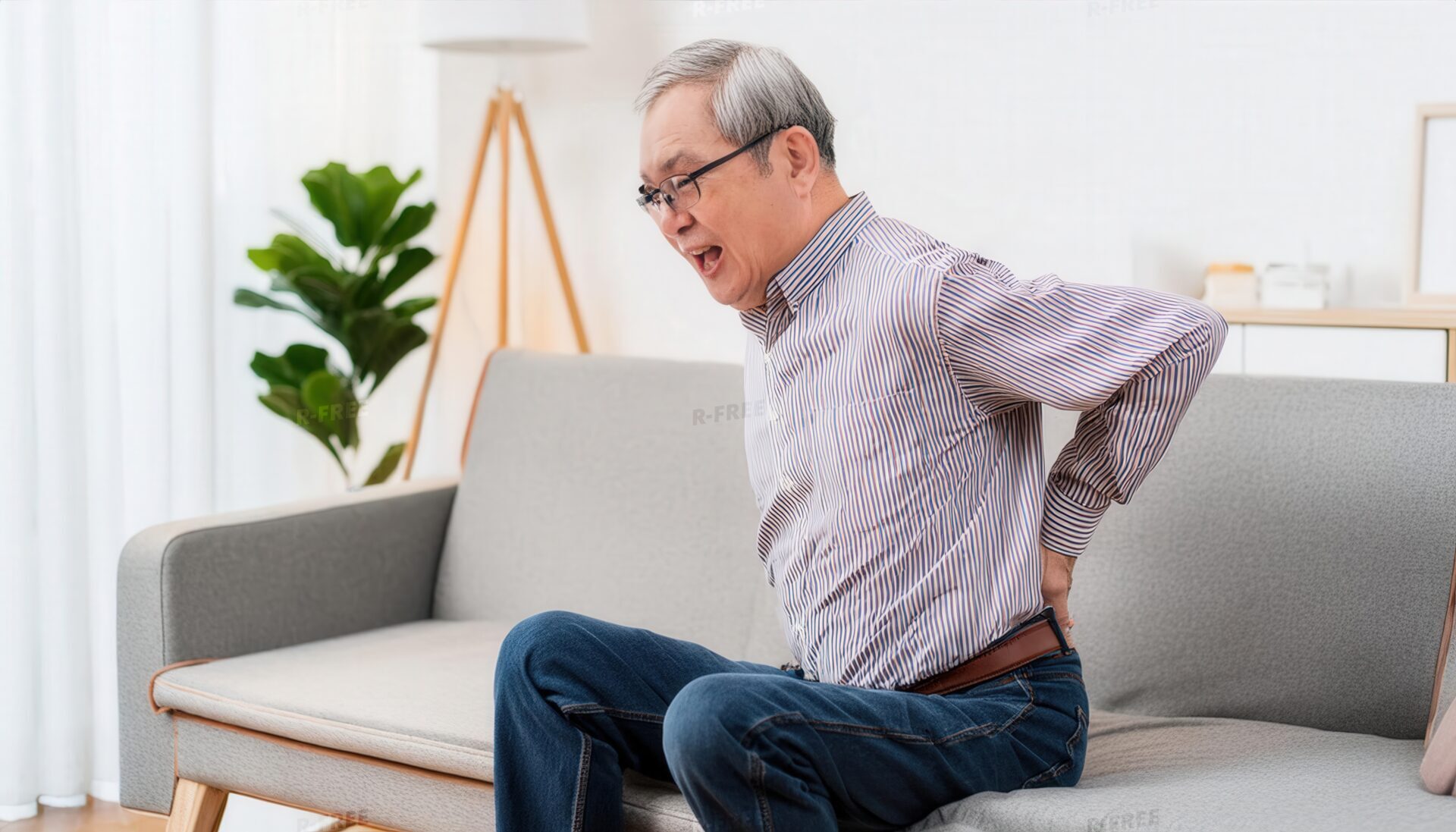 腰痛に苦しむ高齢男性のソファで腰を押さえる表情