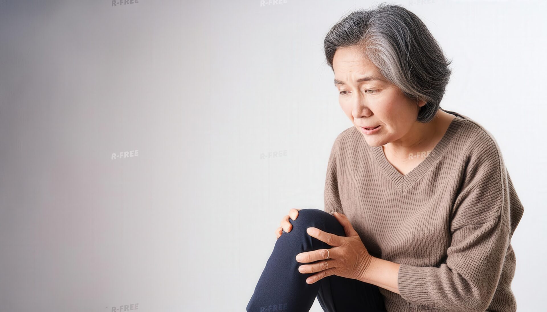 茶色のセーター姿で膝を両手で抱える白髪混じりの高齢女性