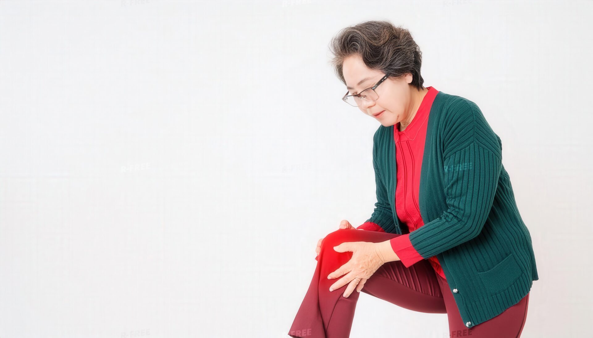 眼鏡姿で赤く強調された左膝を押さえるカーディガンの高齢女性