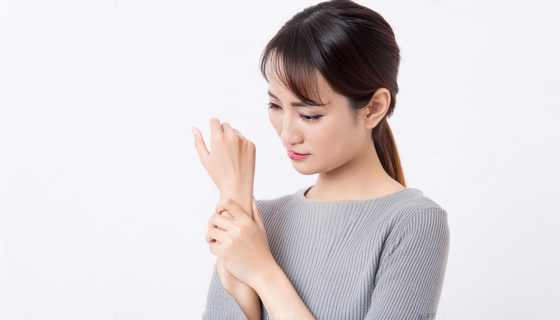 グレーのリブニットで左手首を押さえる痛みに耐える女性