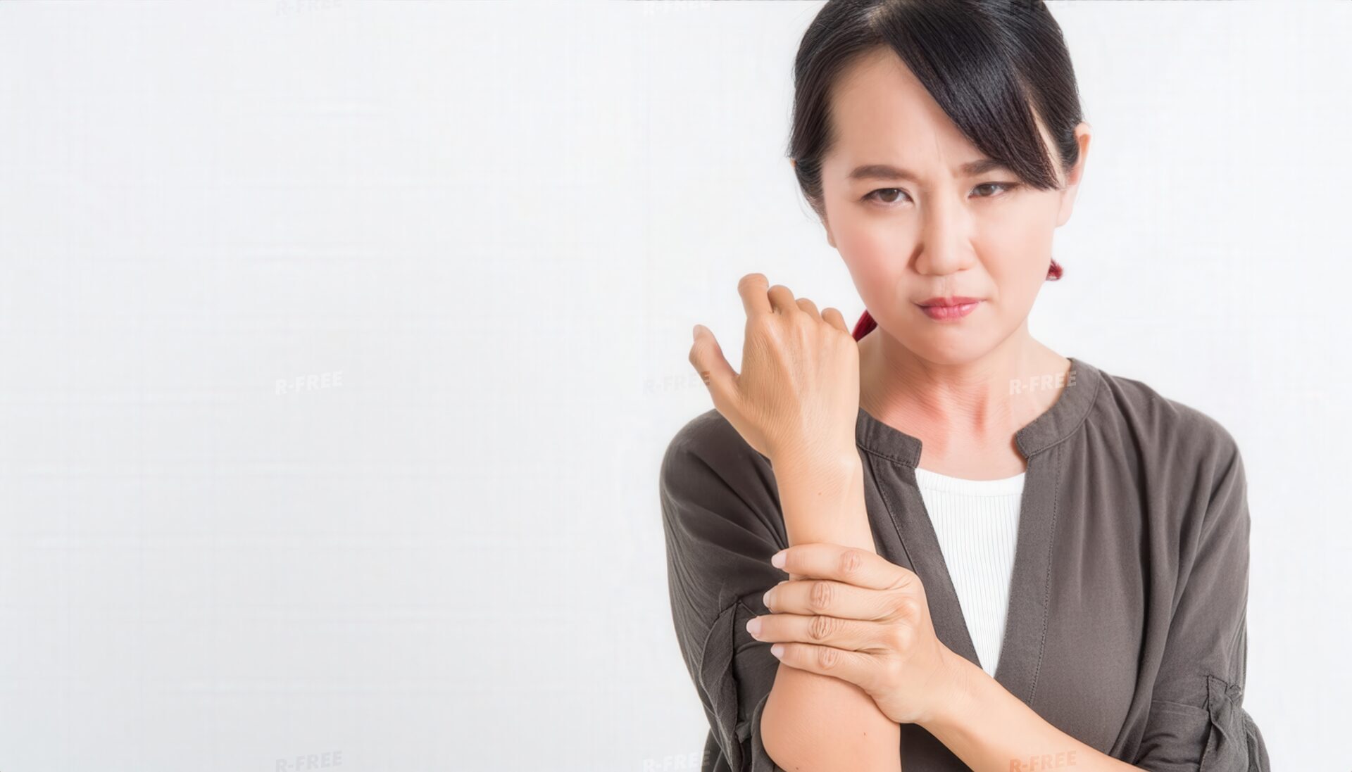 白壁を背景に左手首を押さえて痛みに耐える女性