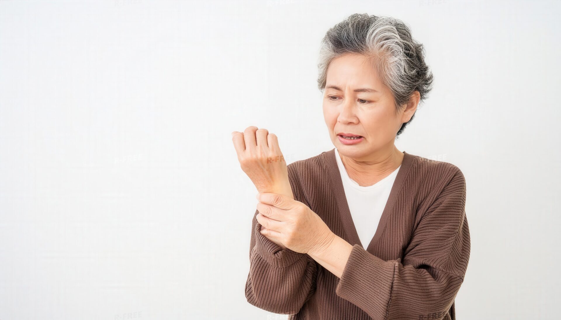 茶色カーディガンで左手首を押さえる苦痛のおばあさん
