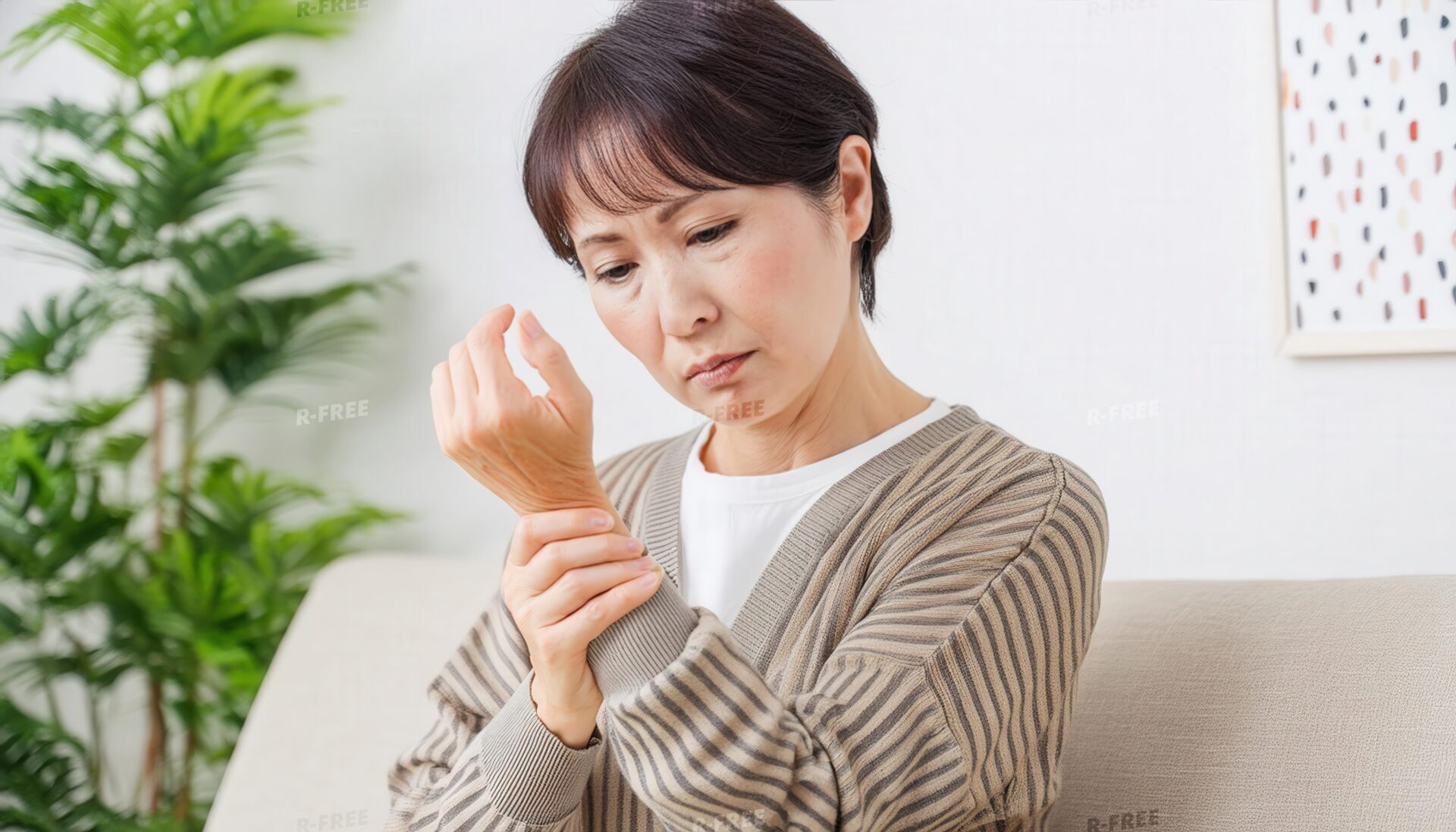 リビングで左手首を押さえる茶色カーディガンの女性