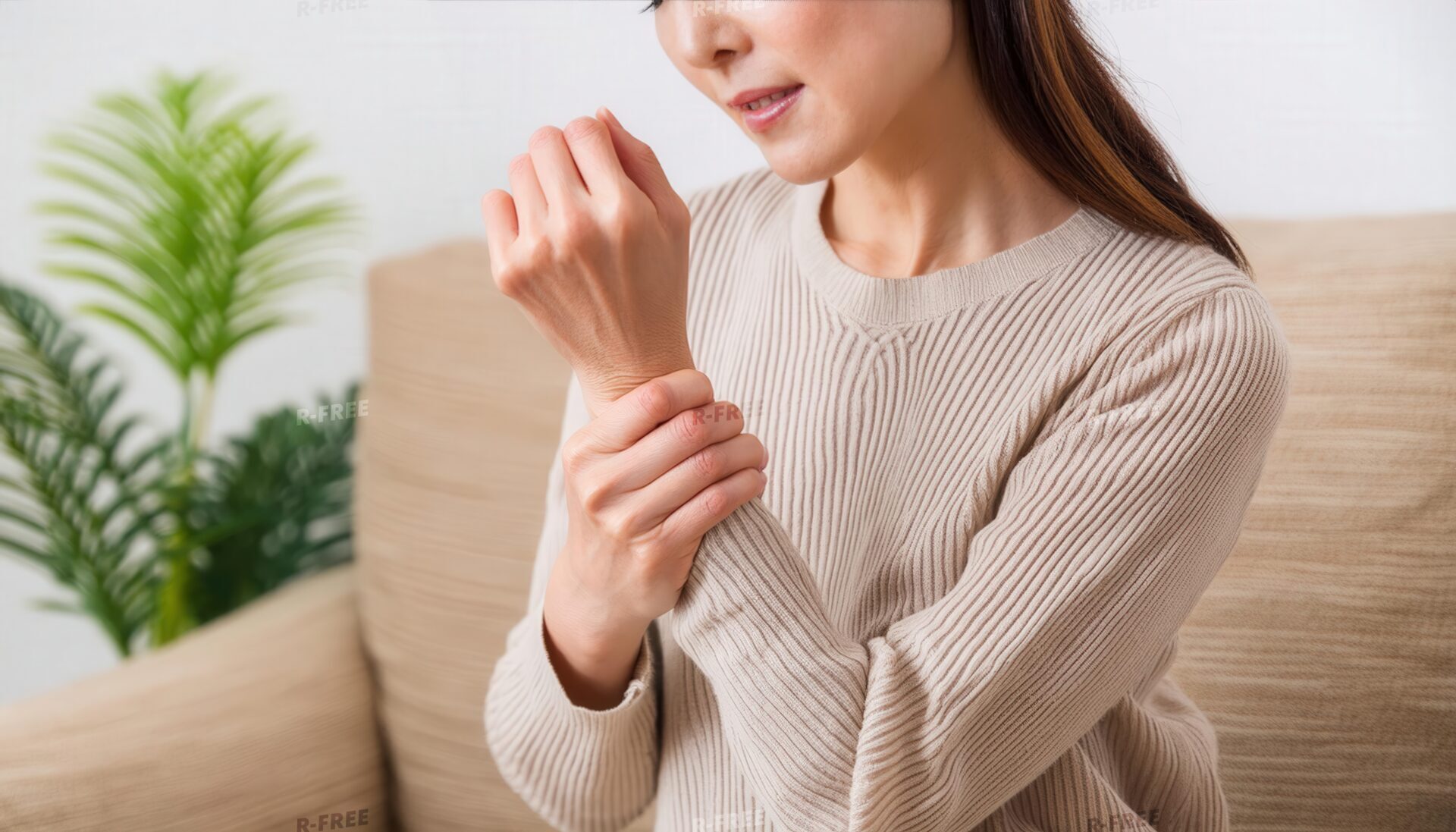 ベージュニットで左手首を押さえる茶髪の女性